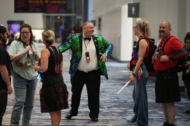 A group of people in colorful and unique attire are gathered in a spacious indoor area, engaging in conversation