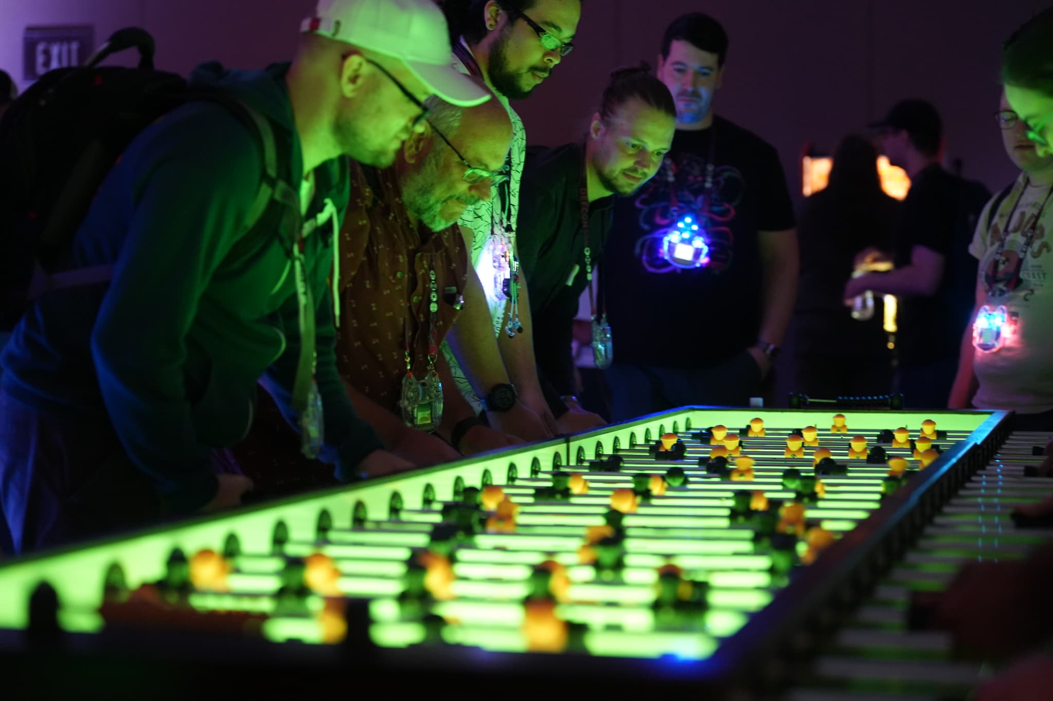 People gathered around a large, illuminated foosball table, engaged in a game