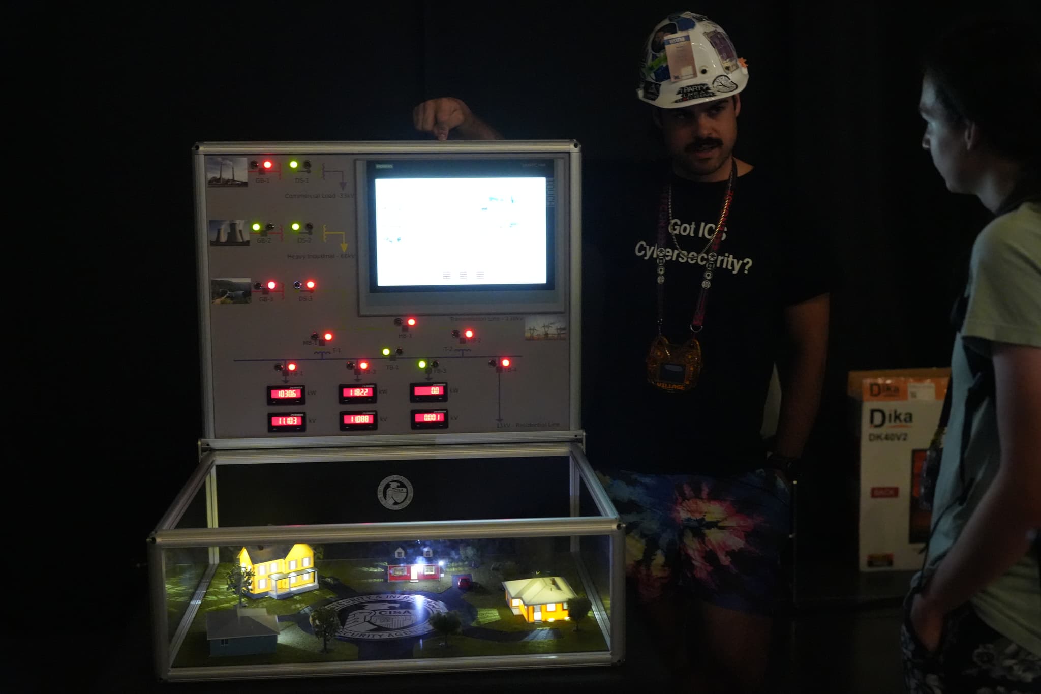 Two people standing near a large electronic device with a screen and various buttons and lights, with a transparent compartment at the bottom displaying objects