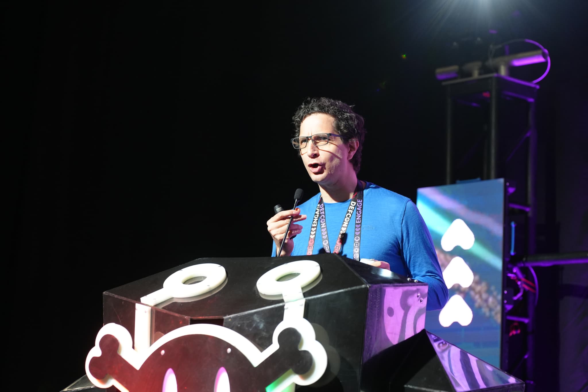 A person speaking passionately at a podium decorated with a stylized skull and crossbones, under stage lighting