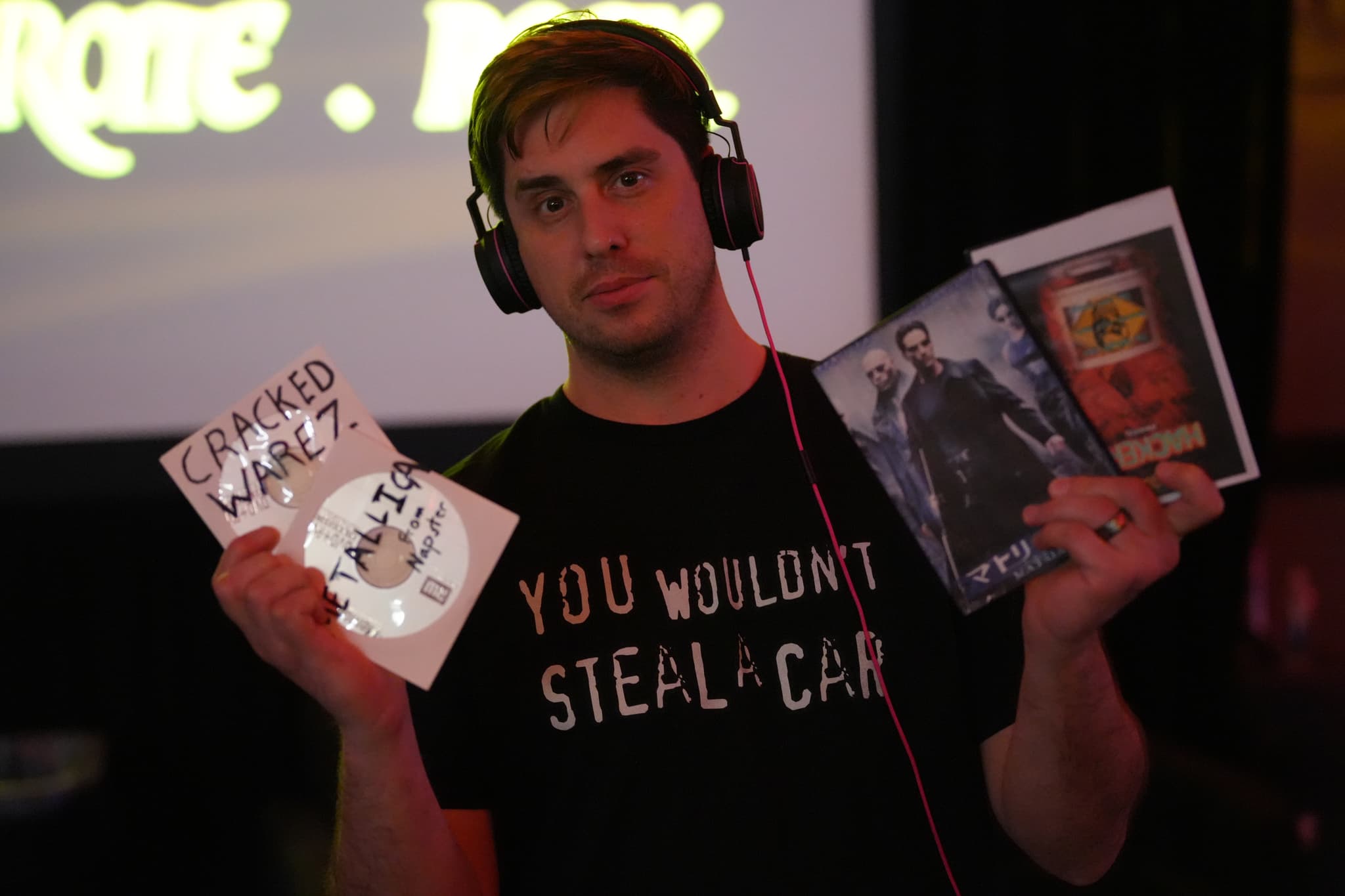 A person wearing headphones and a black shirt with the text YOU WOULDN'T STEAL A CAR is holding a DVD labeled GRAND THEFT WALRUS in one hand and two other DVDs in the other hand