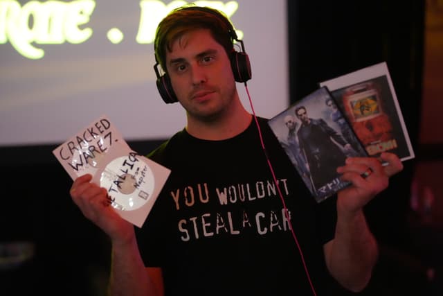 A person wearing headphones and a black shirt with the text YOU WOULDN'T STEAL A CAR is holding a DVD labeled GRAND THEFT WALRUS in one hand and two other DVDs in the other hand