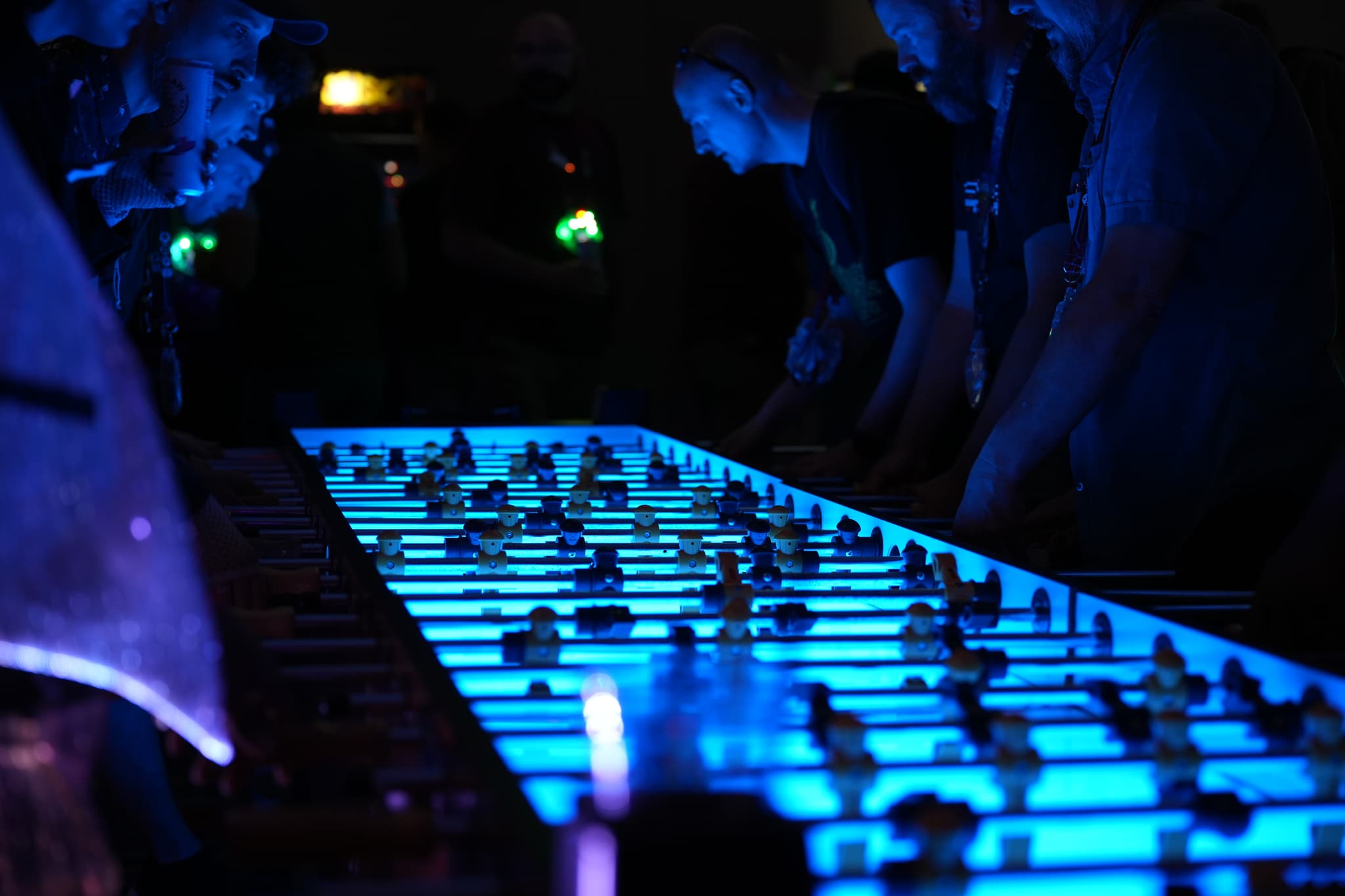 People playing foosball on a large, illuminated table in a dimly lit environment