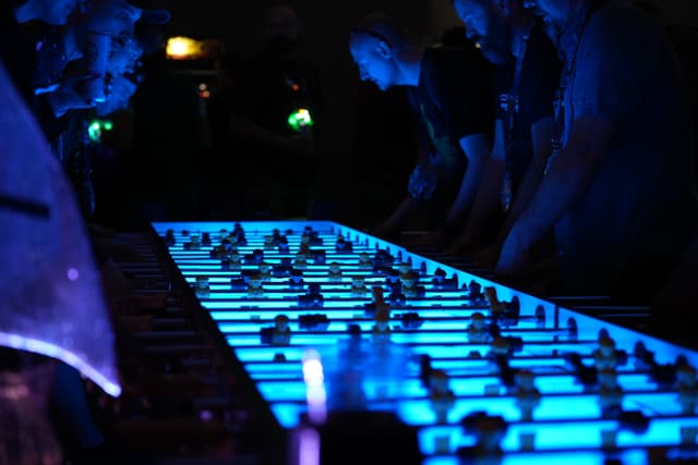 People playing foosball on a large, illuminated table in a dimly lit environment