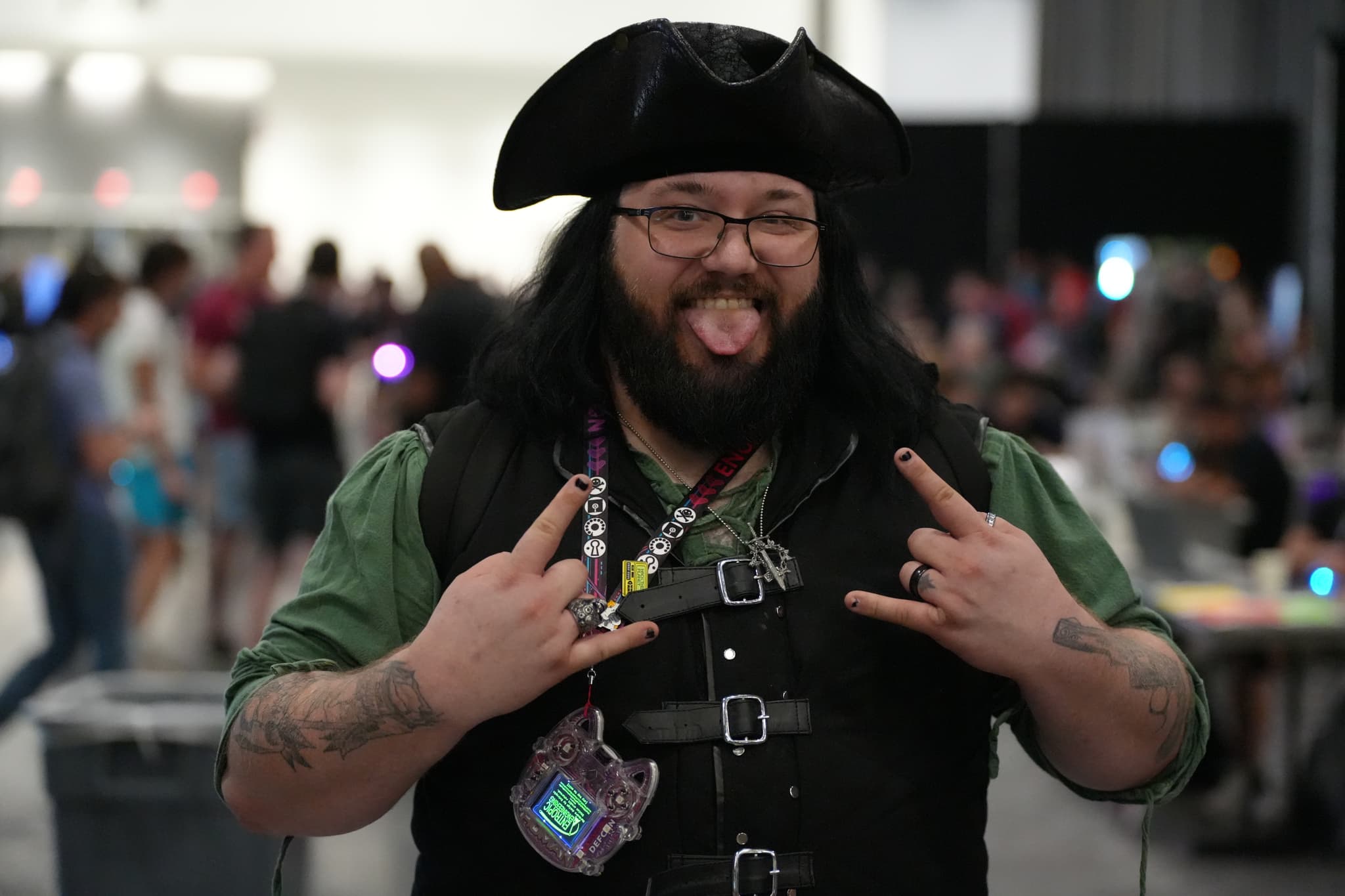 A person dressed in a pirate costume, making a playful gesture with their tongue out and hands forming rock and roll signs, standing in a crowded indoor setting