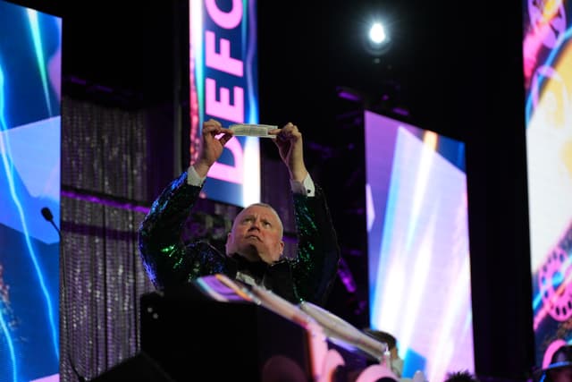 A person on stage holding up an object, with colorful screens and lights in the background