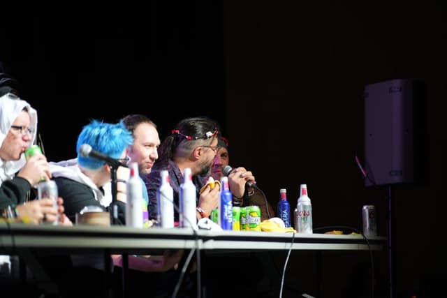 A group of people in costumes sitting at a table with various drinks and microphones, engaged in a discussion or panel