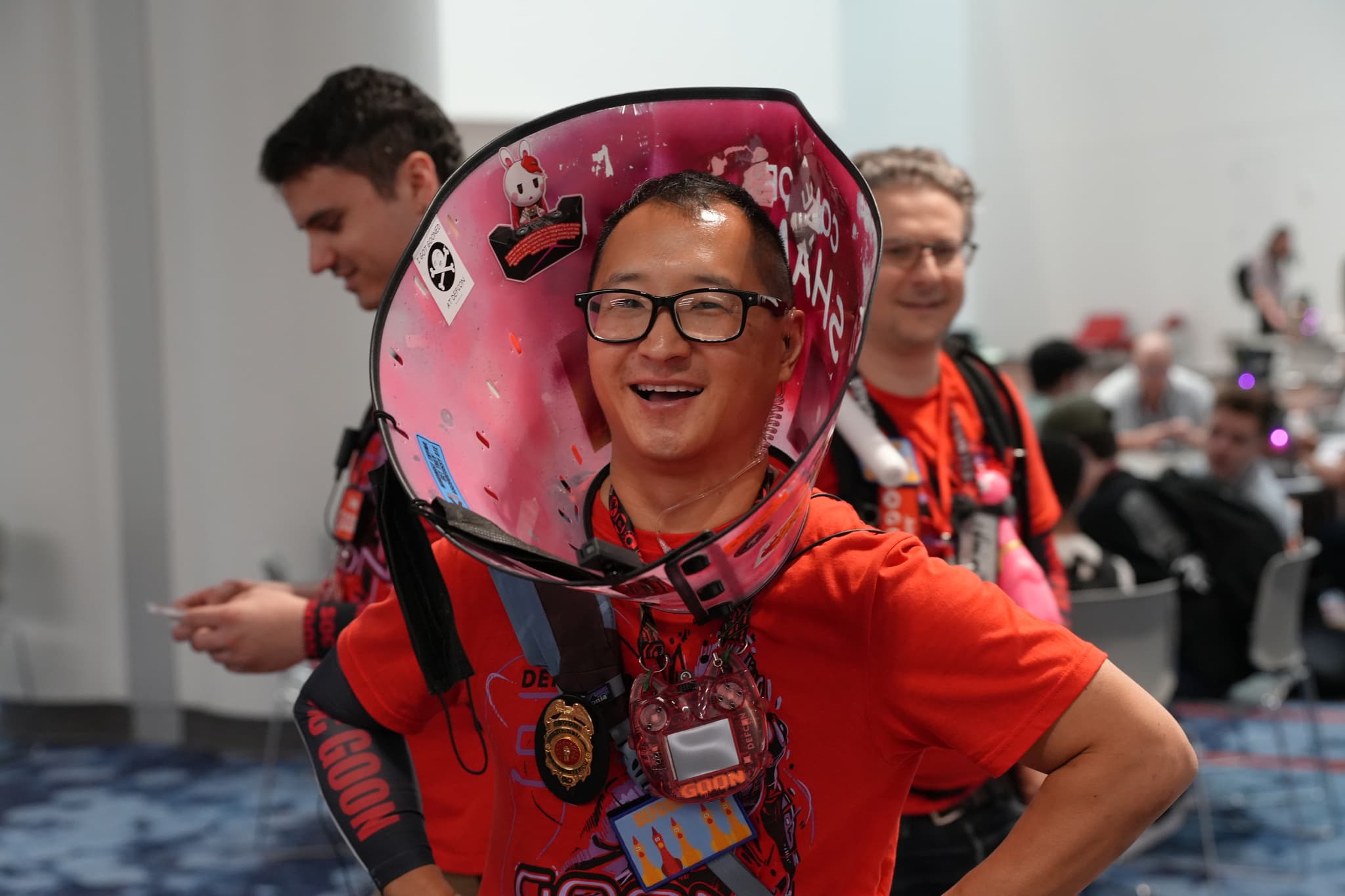 A person wearing a colorful, decorated cone around their neck, smiling, with two other people in the background