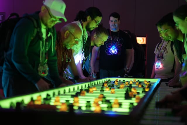 A group of people intensely playing a game of foosball under neon lighting