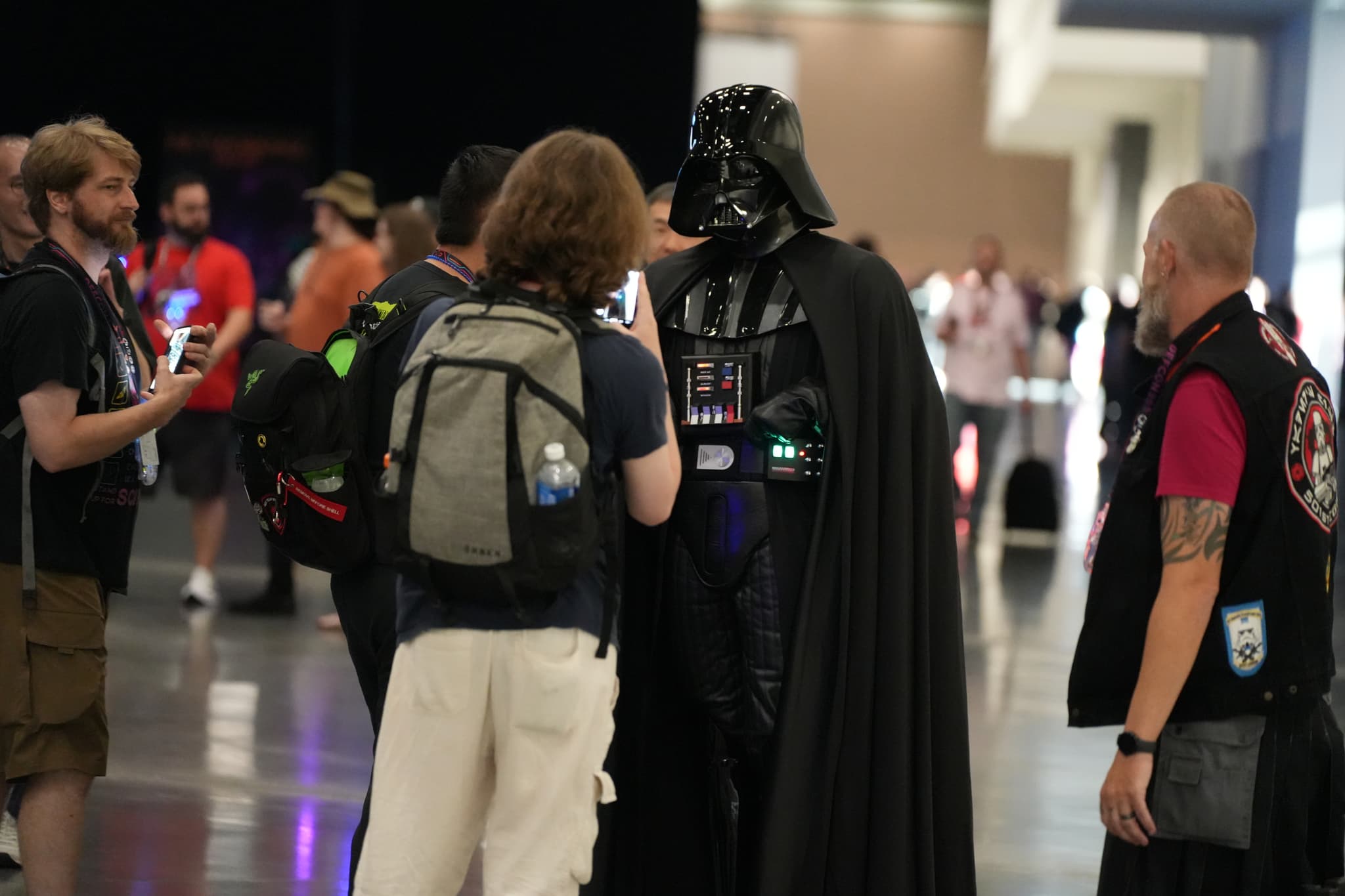 A group of people interacting with someone dressed as Darth Vader at a convention or event