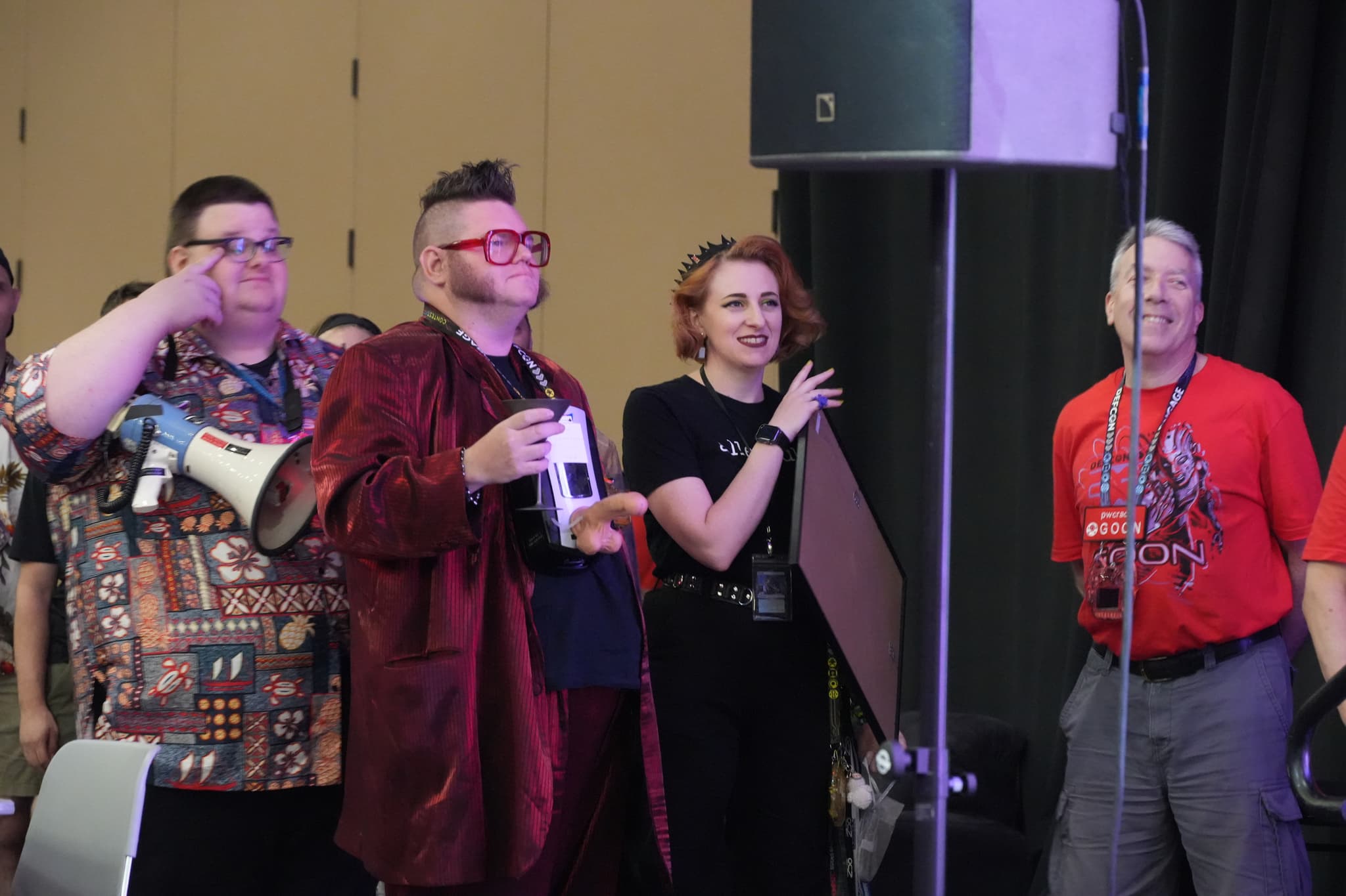 A group of four people standing together, with one person holding a bottle and another person holding a microphone. They appear to be at an indoor event or gathering