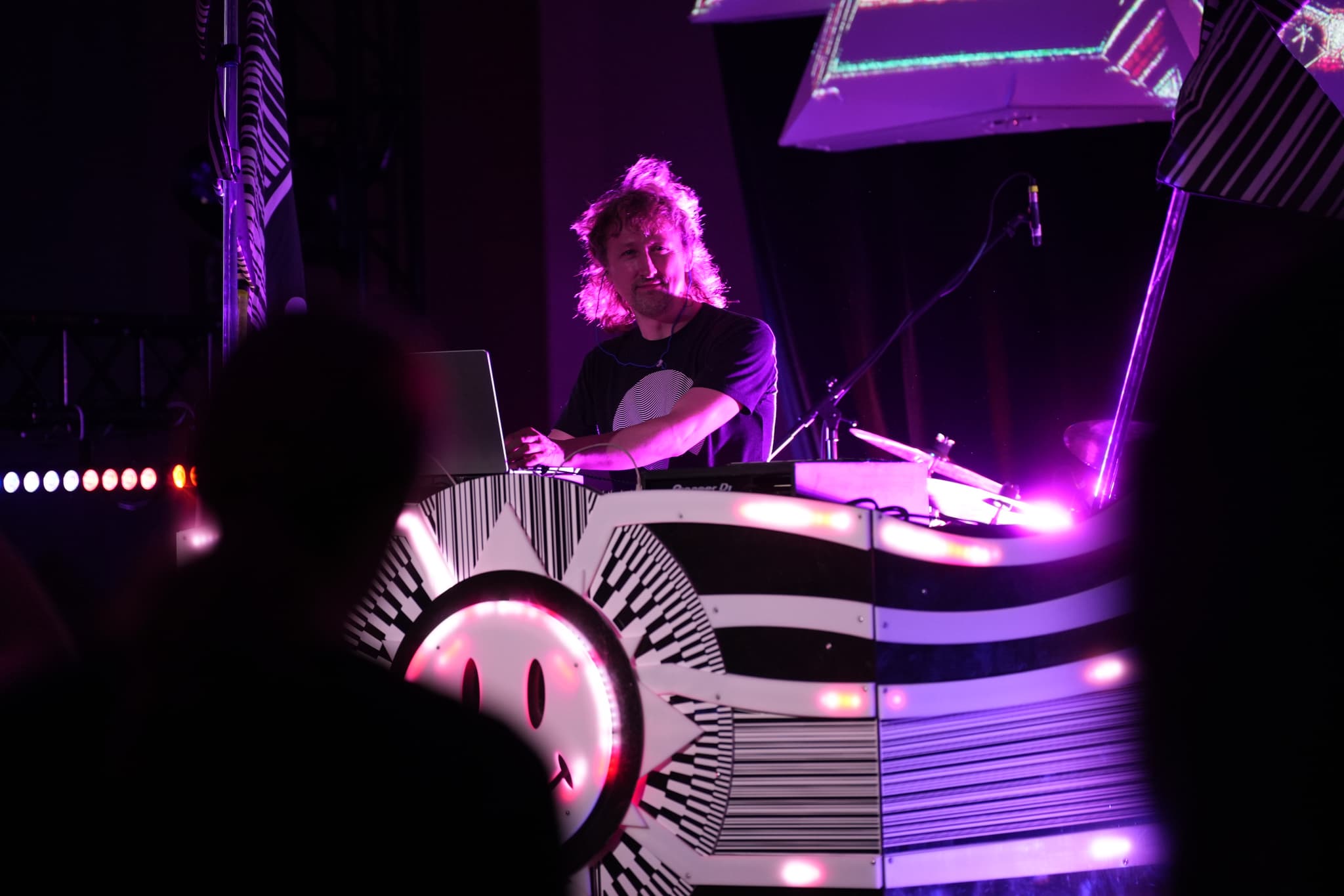 A DJ performing on stage with vibrant purple lighting and a futuristic, illuminated DJ booth