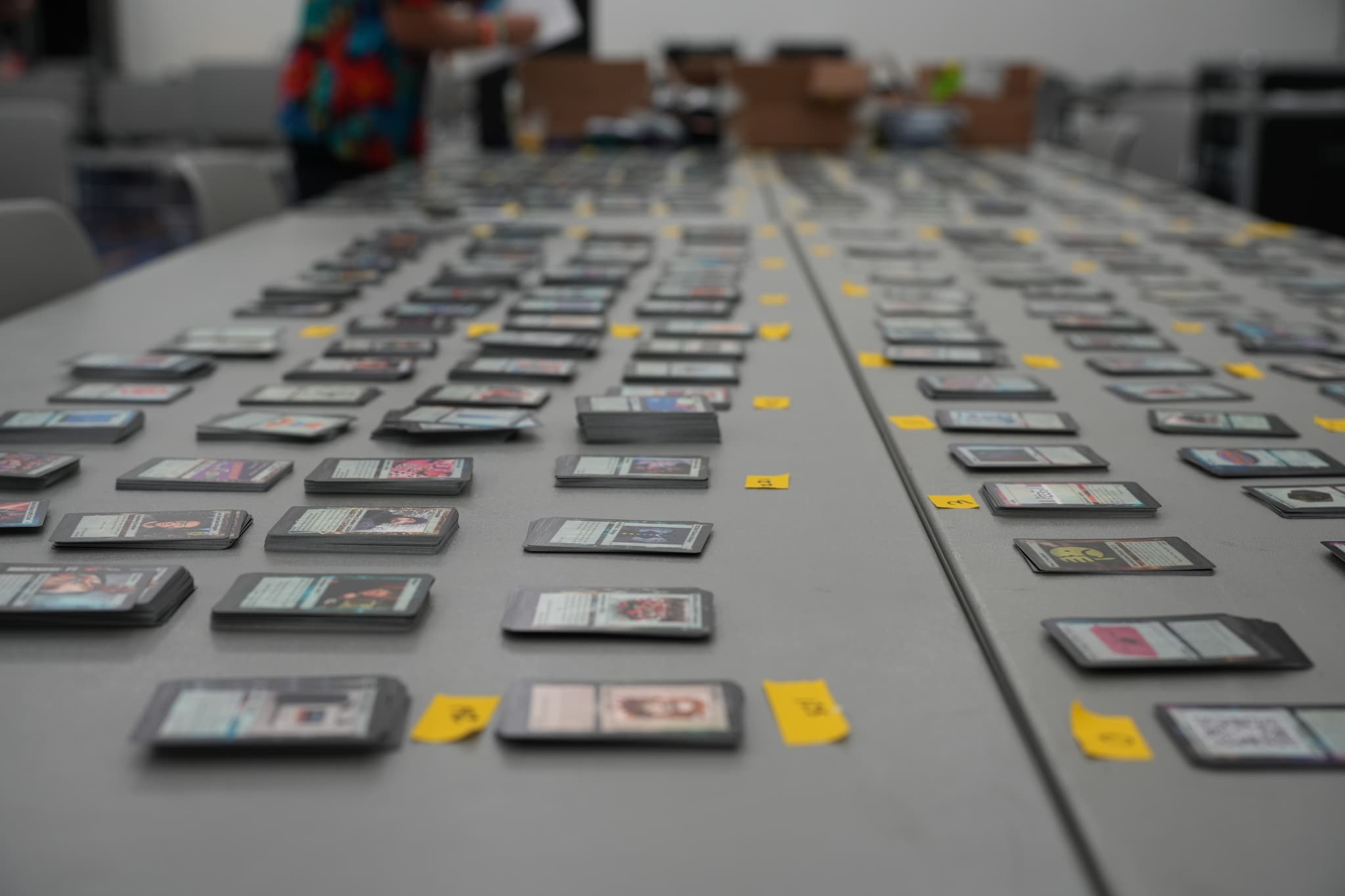 Numerous electronic devices, possibly smartphones or tablets, are arranged in rows on a long table, with yellow tags placed next to each device