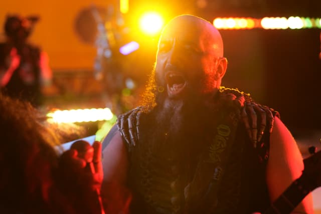 A bearded man passionately singing or shouting on stage, illuminated by vibrant stage lights with a blurred background