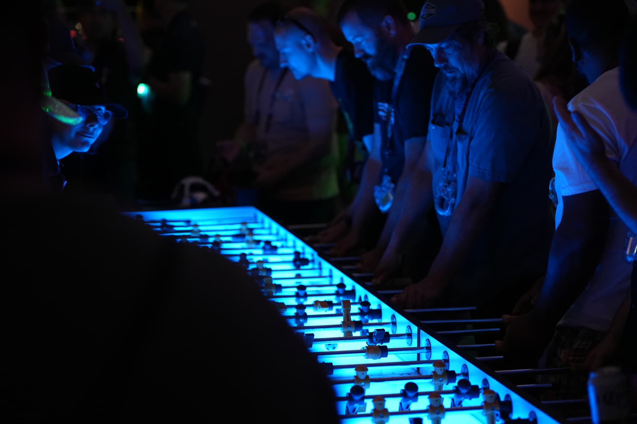 People playing a large, illuminated foosball table in a dimly lit environment