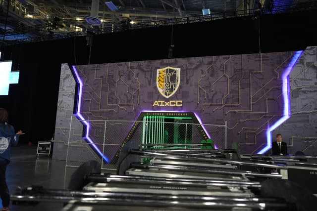 A futuristic stage setup with a large, illuminated backdrop featuring a shield emblem and the text ADMCG. The stage is equipped with various lighting and technical equipment, and there are people in the background