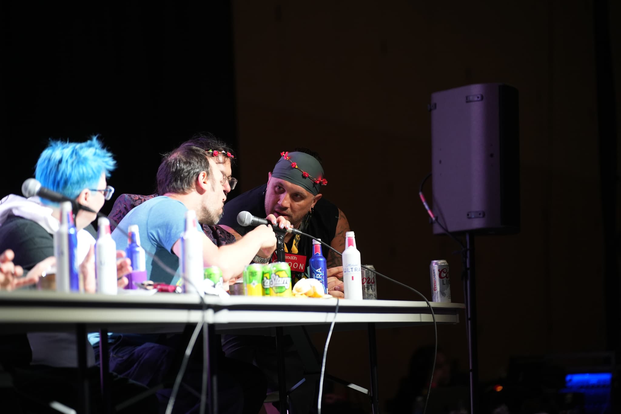 A group of people sitting at a table with various drinks and items, engaged in conversation, with one person holding a microphone