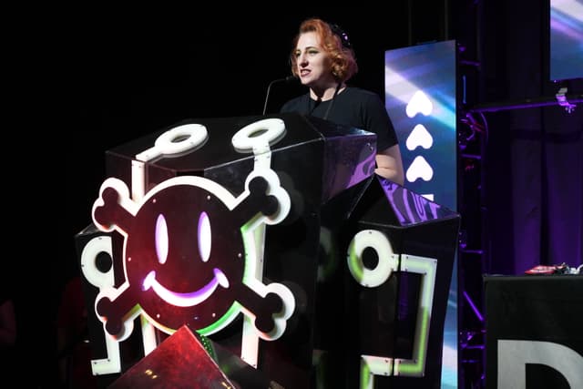 A person standing at a podium decorated with a smiling skull and crossbones symbol, speaking into a microphone