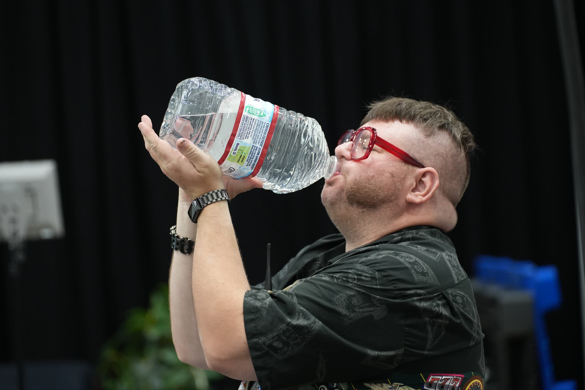 A person with red glasses drinking from a large water bottle