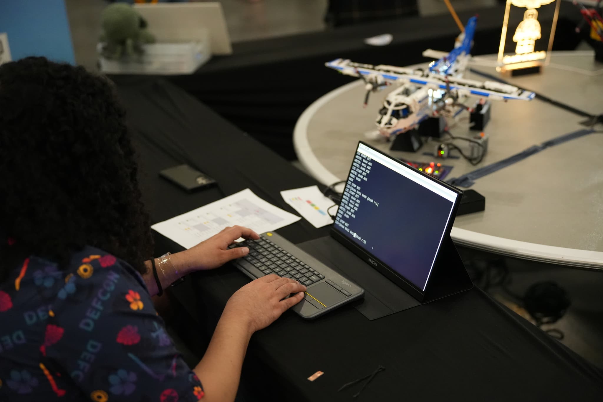 A person working on a laptop with a robotic device on a table nearby