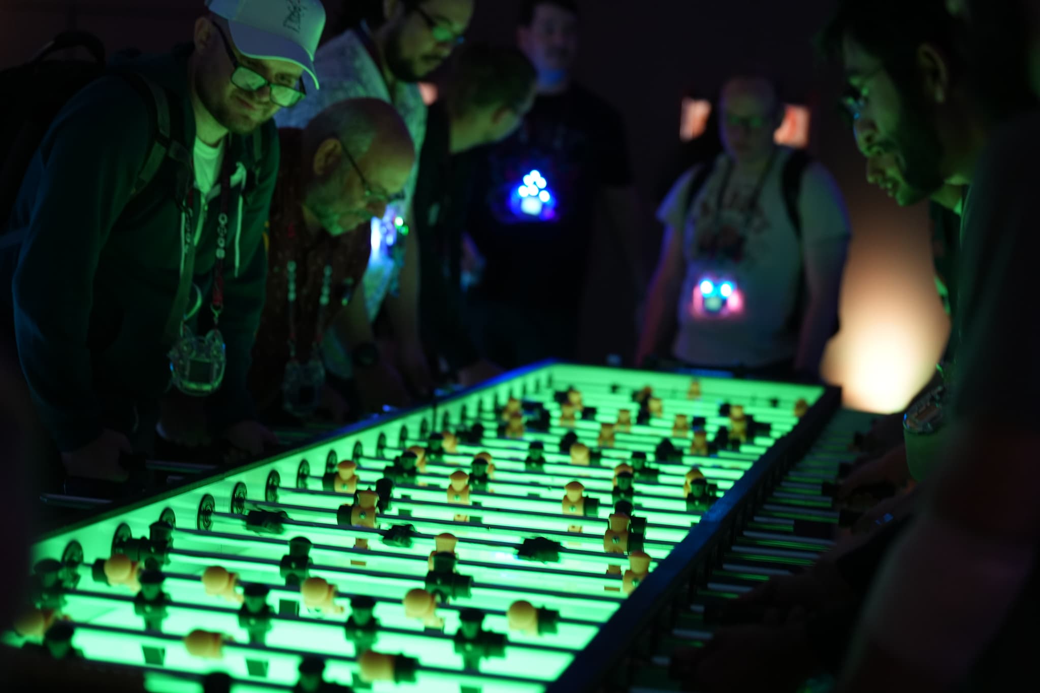 People gathered around a glowing, neon-lit foosball table in a dimly lit room