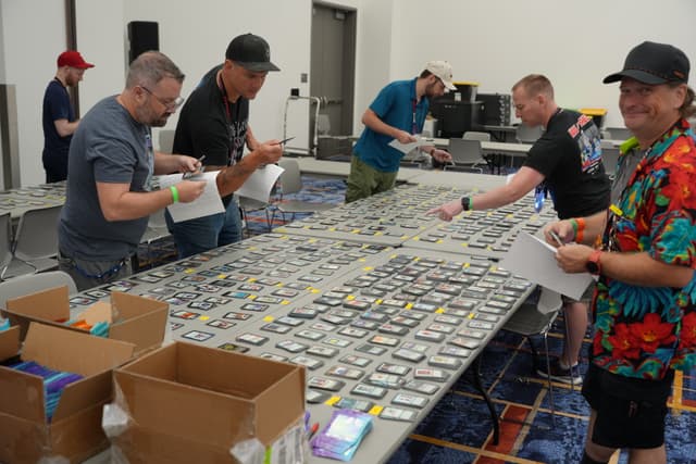 Several people examining and organizing a large collection of video game cartridges on a long table in a room