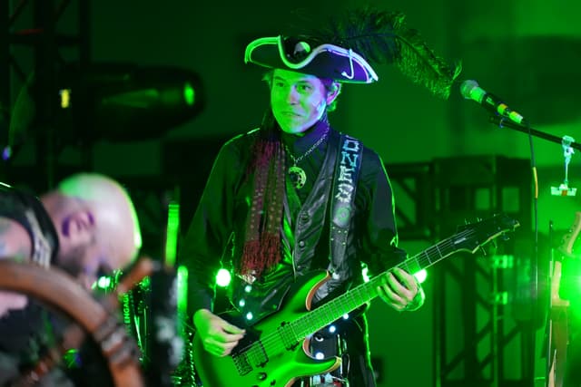 A musician dressed in a pirate-themed outfit playing a guitar on stage, illuminated by green lighting