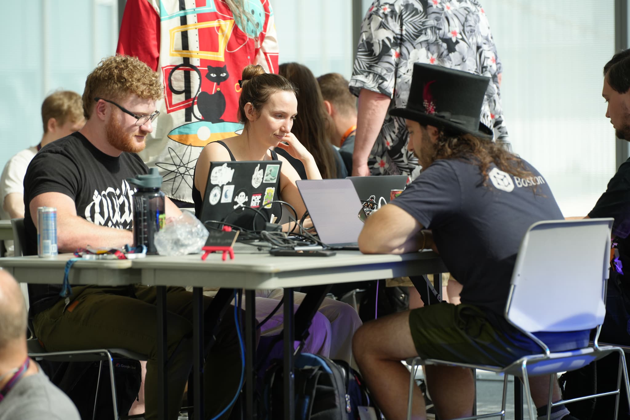 A group of people sitting around a table, working on laptops, with one person wearing a top hat