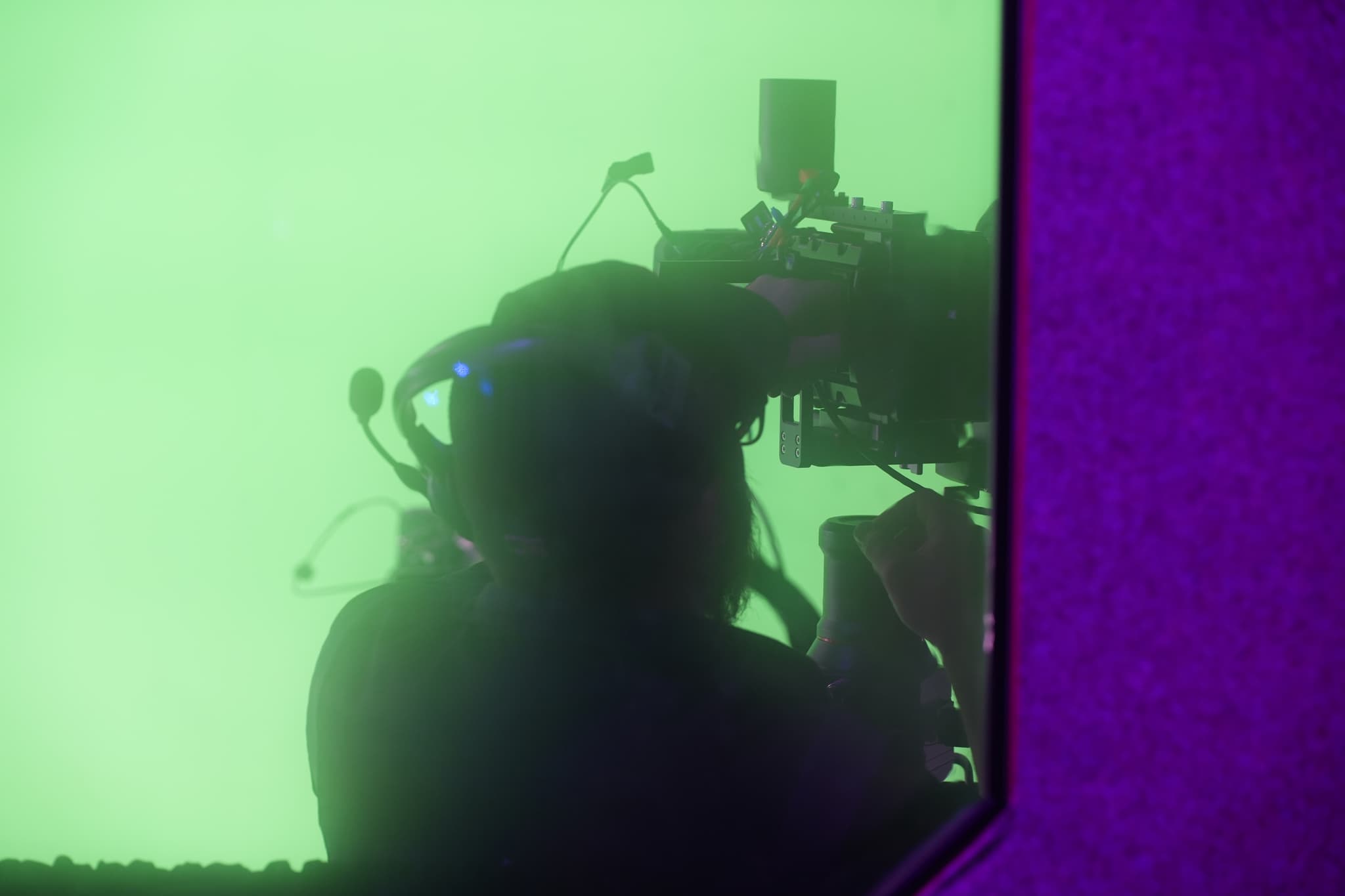 A silhouette of a person operating a camera against a green background, framed by a purple border